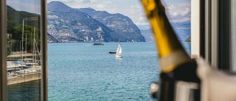 A view of a coastal area with mountains, a sailboat, and a bottle of champagne in the foreground.