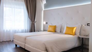 Habitación de hotel moderna con dos camas, un ventanal grande con cortinas translúcidas y un suelo de madera claro.