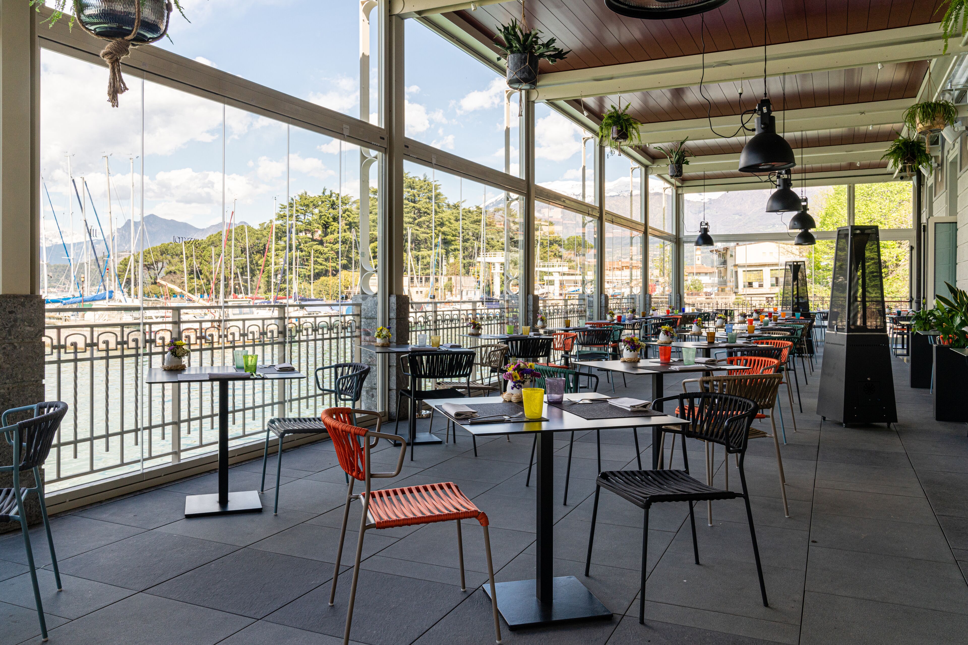 An outdoor dining area with tables and chairs, large windows, and potted plants.
