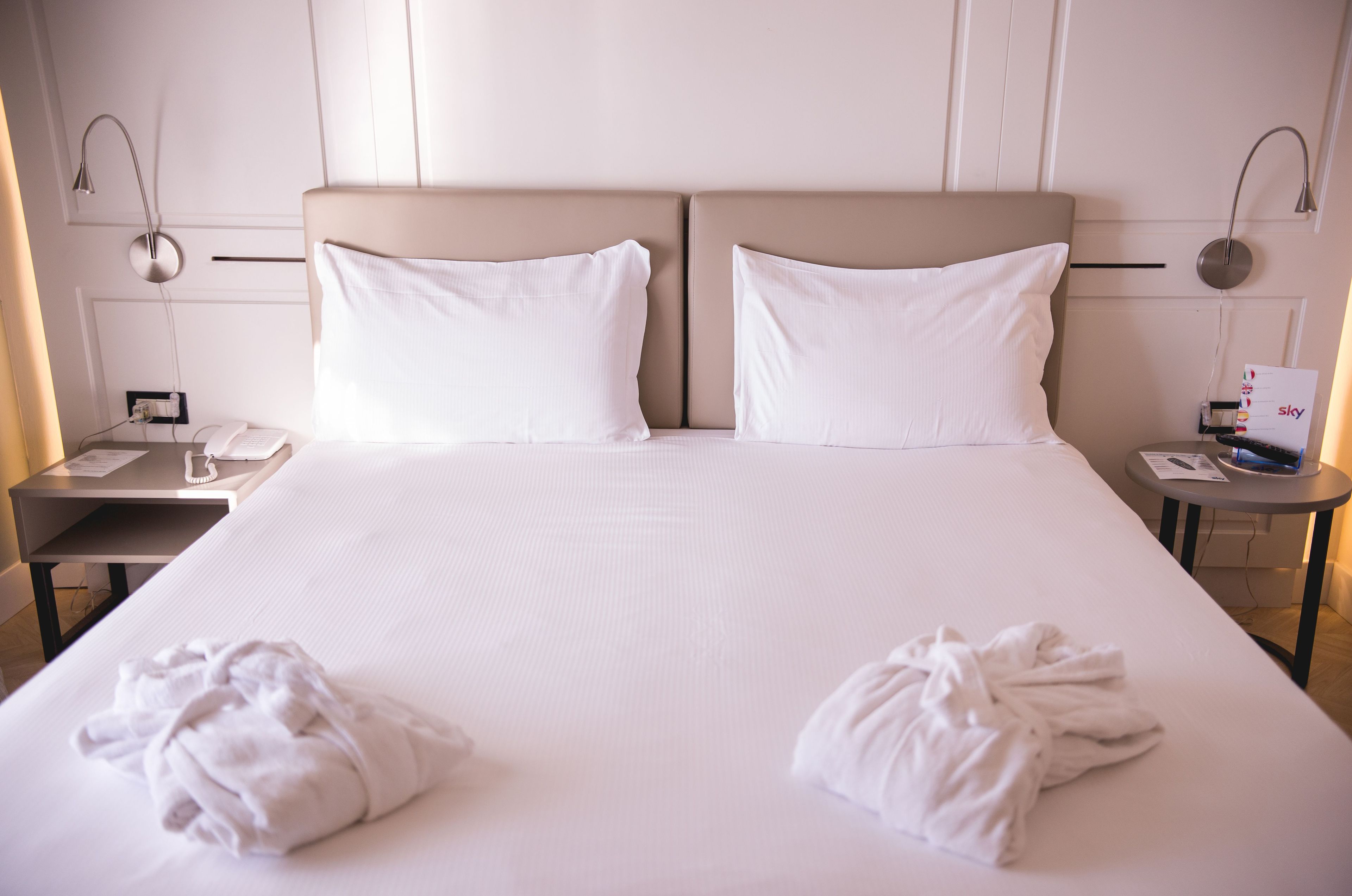 Una habitación de hotel con una cama grande, dos mesitas de noche, una lámpara de noche y un reloj de pared.