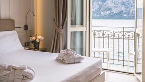 A hotel room with a bed, a nightstand with a lamp, a vase of flowers, and a view of a mountainous landscape through a balcony. - Hotel Araba Fenice (Iseo)