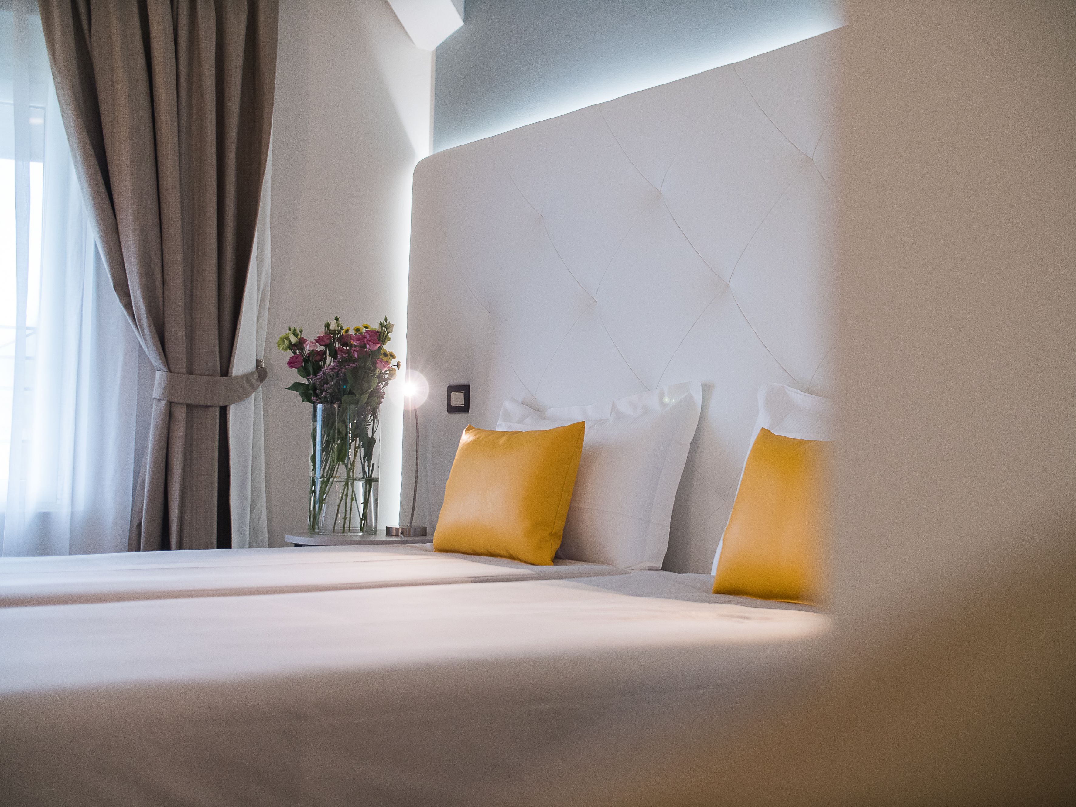 A hotel room with a large bed, a vase with flowers, and a view of the outdoors.