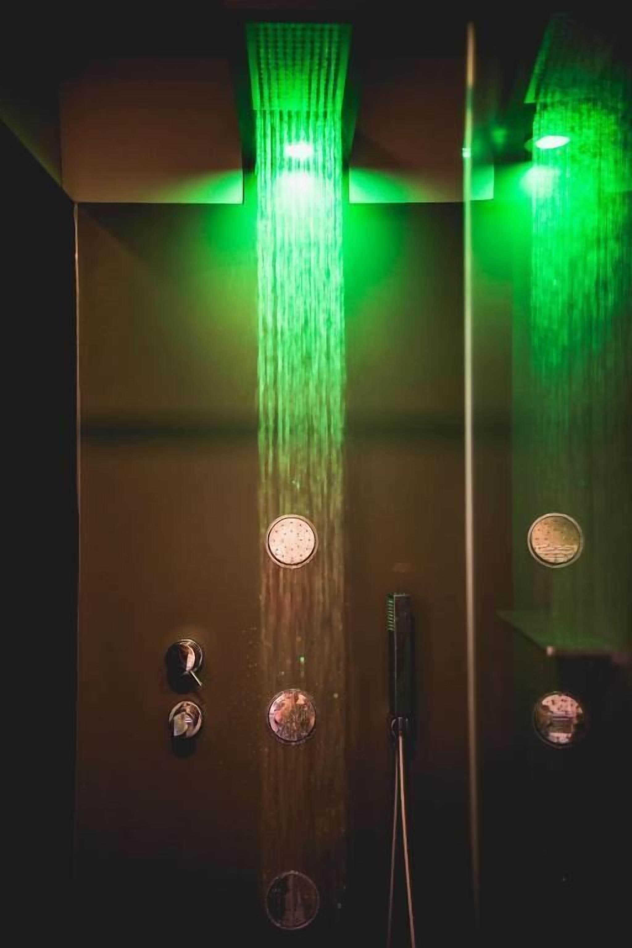 Ducha con múltiples rociadores y cabezal de ducha de mano, iluminada con luz verde.