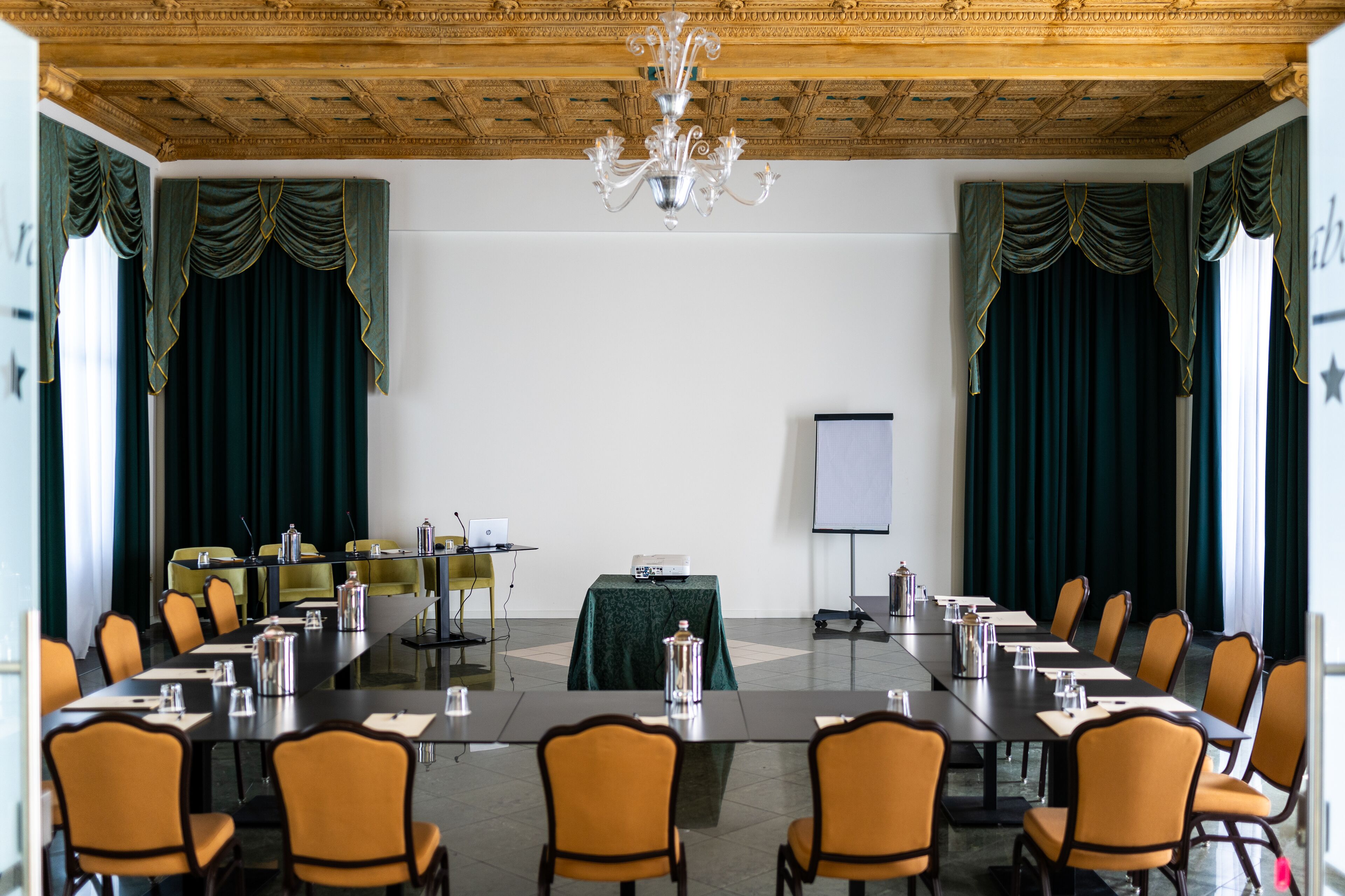 A conference room with a long table, chairs, a projector screen, and a chandelier.