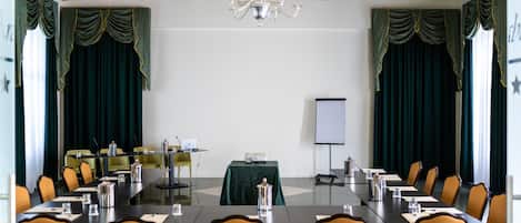 Une salle de conférence avec une longue table, des chaises, un écran de projection et un lustre.