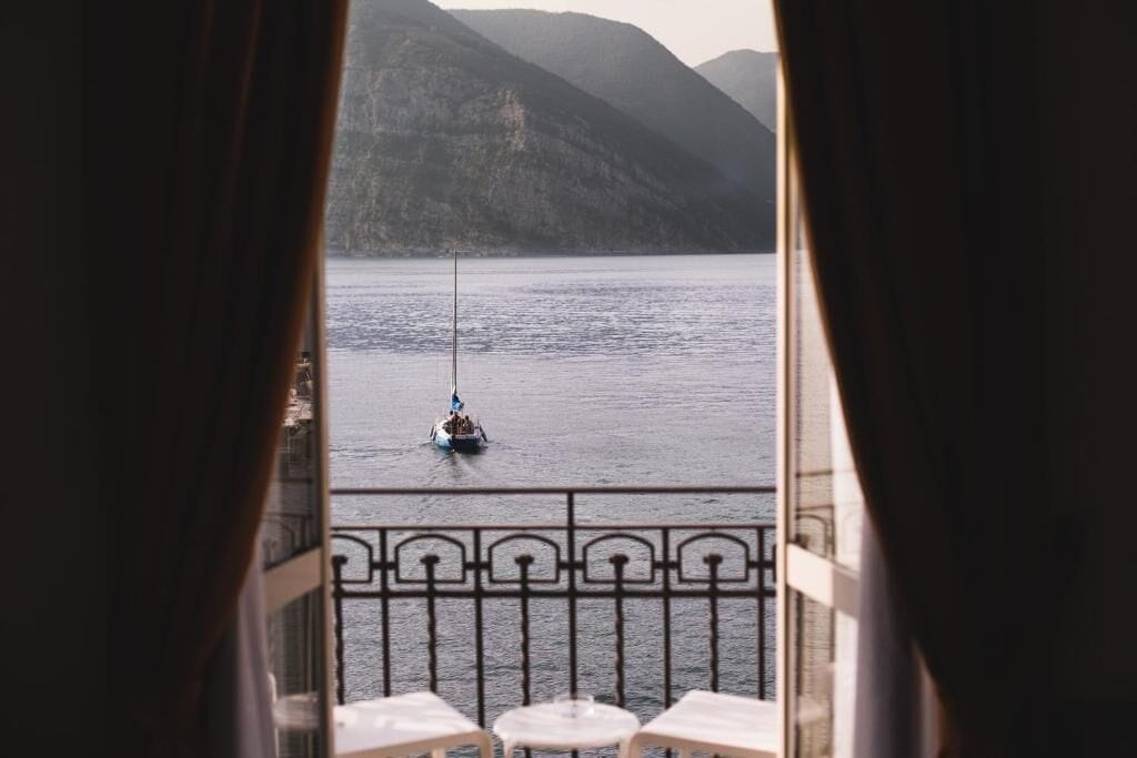 Een balkon met uitzicht op een meer en bergen, een zeilboot en een balustrade.