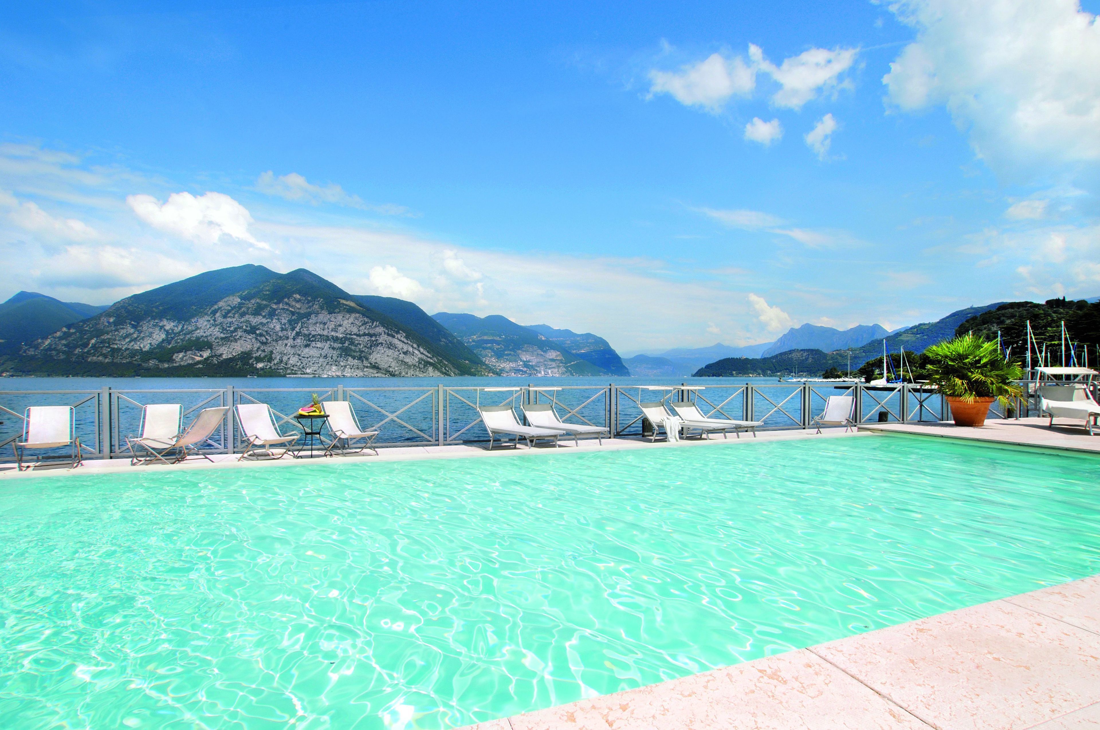 A swimming pool with lounge chairs and a view of mountains and the sea.