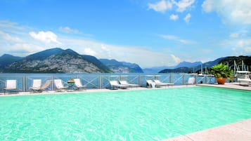 A swimming pool with lounge chairs and a view of mountains and the sea.