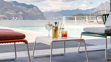 A terrace with a table set for two, overlooking a body of water and mountains.