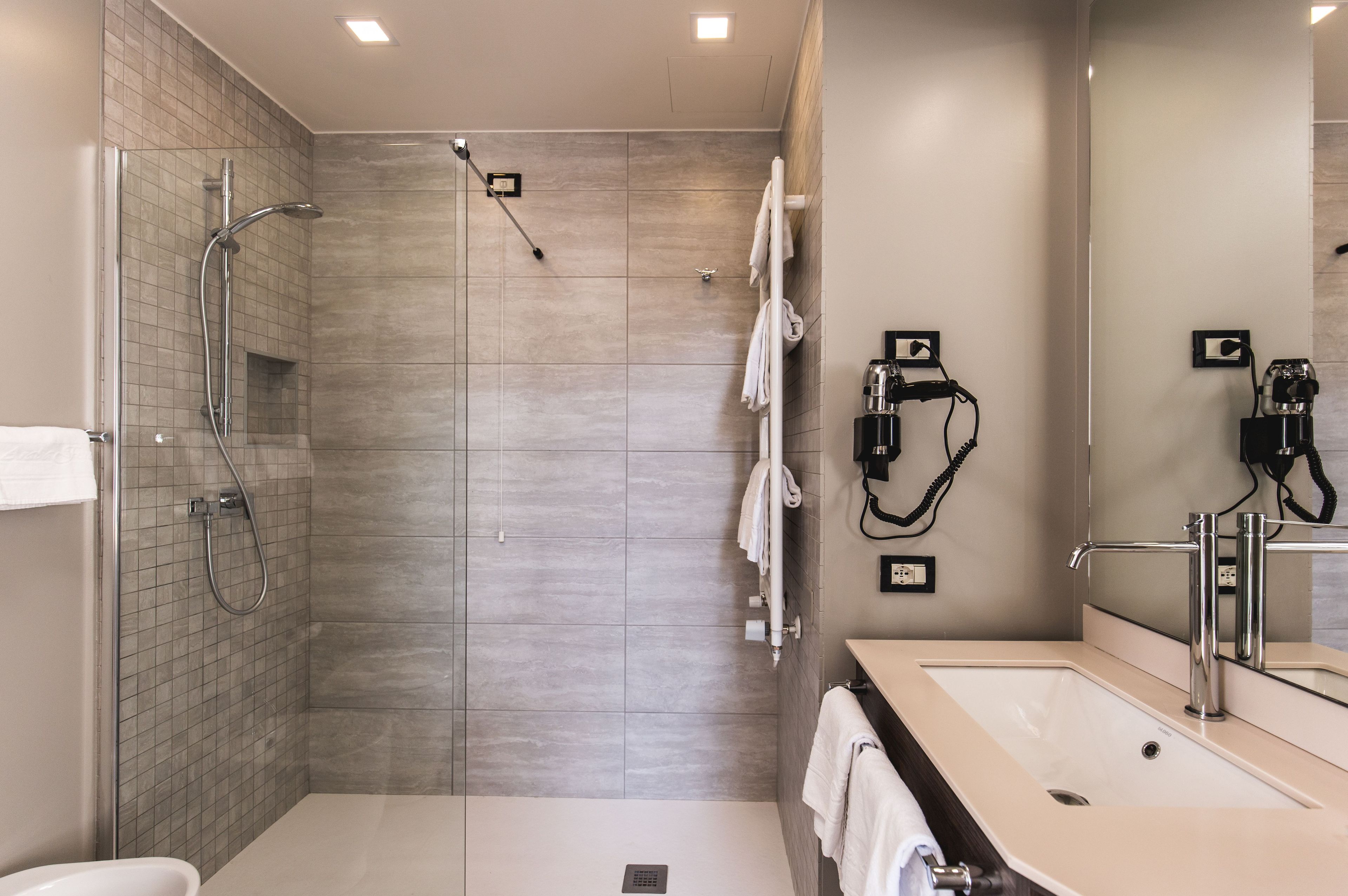 Ein modernes Badezimmer mit einer gläsernen Duschkabine, einem Waschbecken mit Spiegel und Handtuchhaltern.