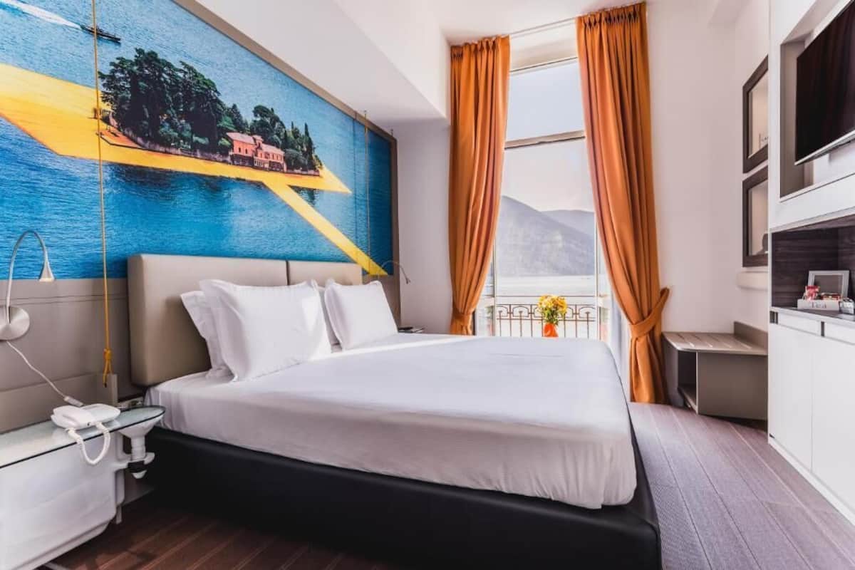 Une chambre d’hôtel avec un lit, un tableau, une télévision et une fenêtre avec des rideaux.