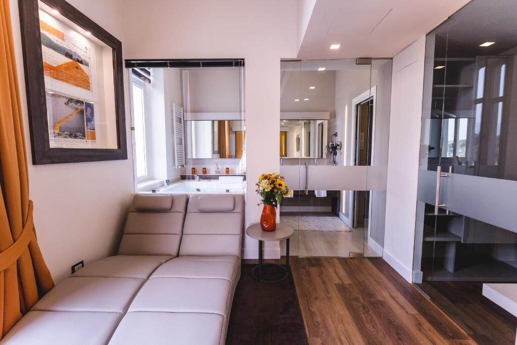 A modern interior with a sofa, a small table with a vase, and a kitchen area visible through a glass partition.