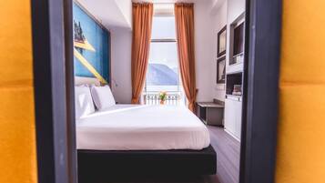 Habitación de hotel con cama, escritorio, silla, ventana con cortinas y un cuadro en la pared.