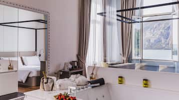 A modern hotel room with a bed, a vanity with a mirror, a window with a mountain view, and a balcony with a view of the mountains.