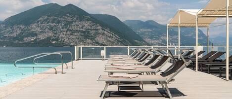 A poolside area with sun loungers, a pool, and a view of mountains.