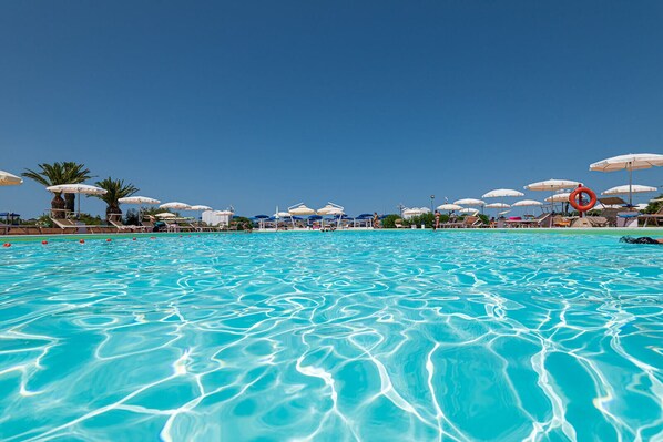 Una piscina al aire libre, sombrillas, sillones reclinables de piscina