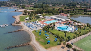 Luchtbeeld van een resort met zwembad, strand en tennisbaan.
