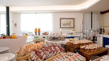 A buffet setup with various food items, including vegan options, and a large window providing natural light.