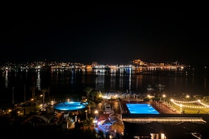 Un hotel frente al agua con piscina, un puerto deportivo y un paisaje urbano al fondo.