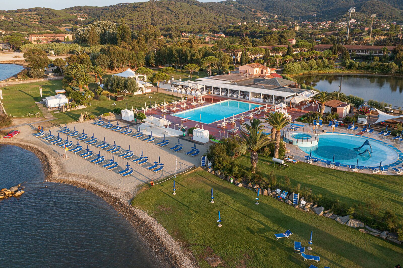 Vista aérea de un complejo turístico con varias piscinas, tumbonas y una zona de playa.