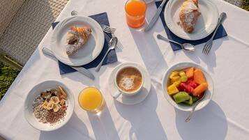 A table set outdoors with breakfast items including croissants, fruit, cereal, and coffee.