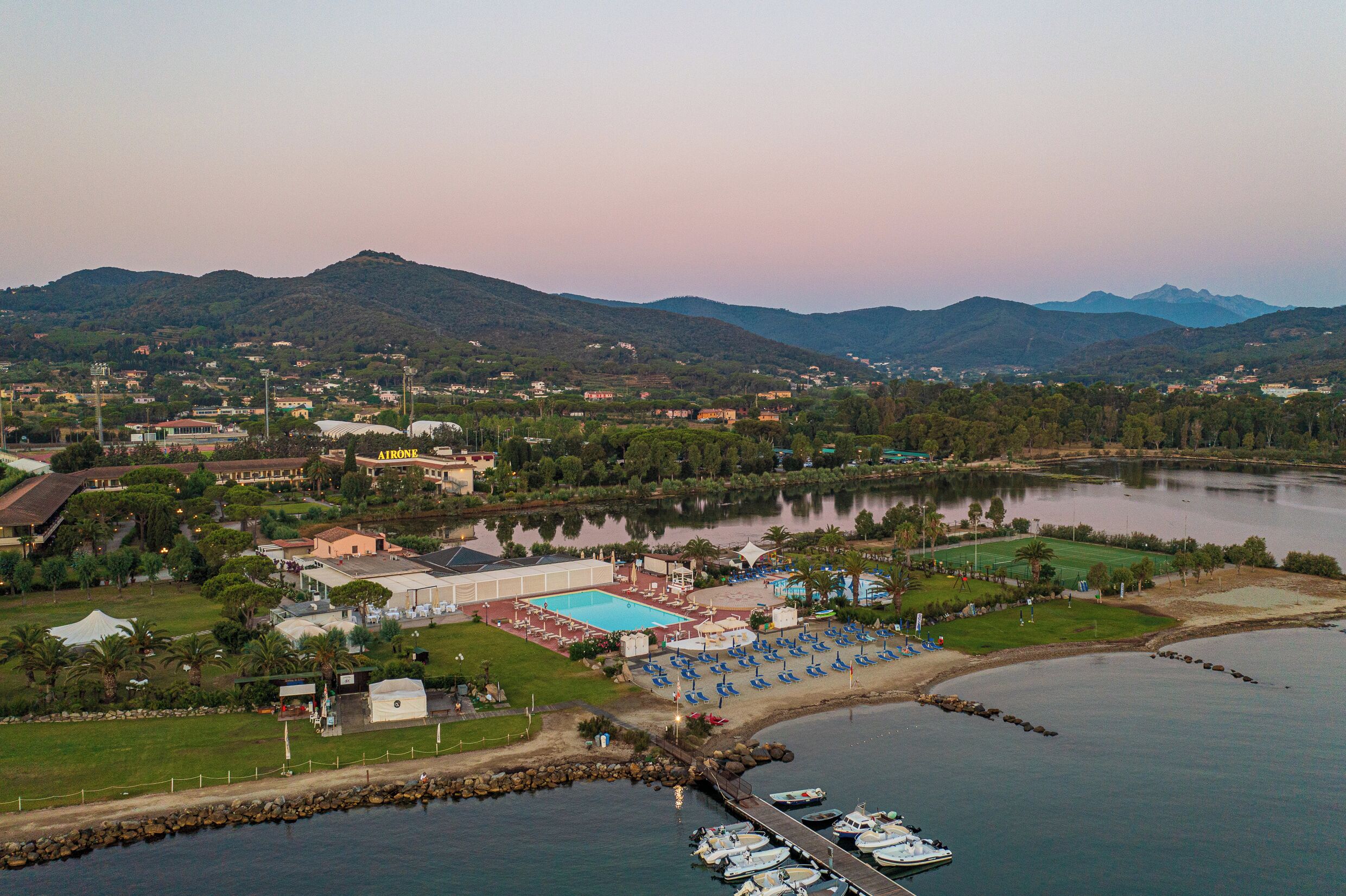 An aerial view of a resort with a swimming pool, beach area, and boats docked at the marina.