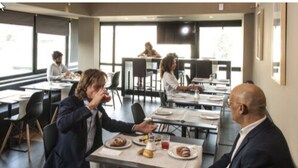Un comedor moderno con mesas y sillas, ventanas amplias y un ambiente relajado.
