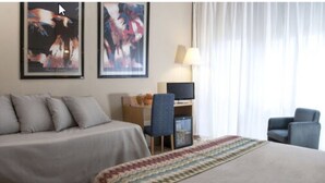 Habitación de hotel con cama, escritorio con silla, lámpara y dos cuadros abstractos en la pared.