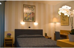 A hotel room with a bed, a desk, a chair, a lamp, and a painting on the wall. - Hotel Clarici (Spoleto)