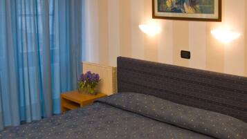 Een hotelkamer met een bed, nachtkastje, lamp en een schilderij aan de muur.