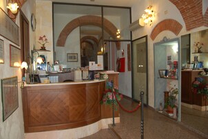 Zona de recepción con mostrador de madera, una barrera de cuerda roja y un espejo que refleja el interior.