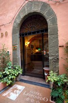 Entrada de hotel con un arco, felpudo con el nombre del hotel y plantas en macetas a ambos lados.