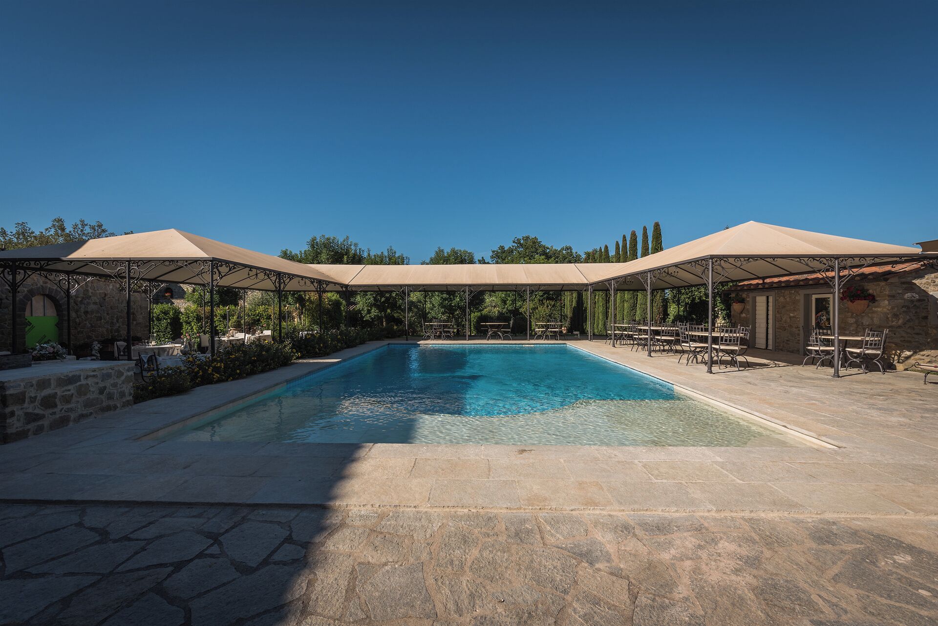 A swimming pool with a stone deck, surrounded by covered seating areas and stone walls.