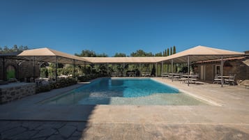 A swimming pool with a stone deck, surrounded by covered seating areas and stone walls.