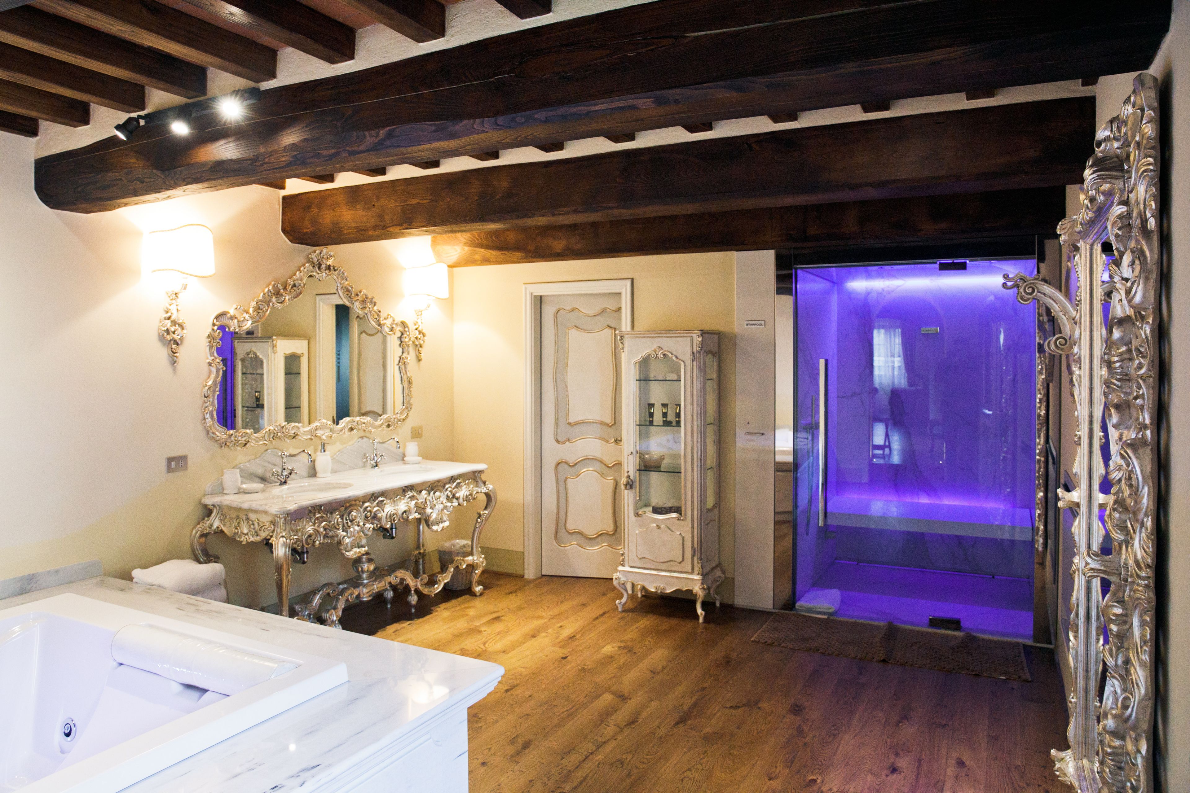 Une salle de bain dotée d’un lavabo en marbre, d’un miroir décoratif et d’une douche à l’italienne avec un éclairage violet.