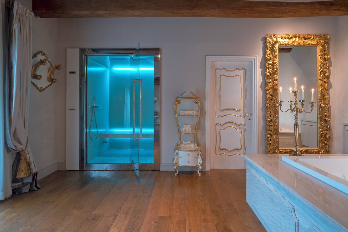 A bathroom with a glass shower enclosure, a vanity with a gold-framed mirror, and a white cabinet.