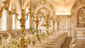 A long banquet table with gold candelabras, white flowers, and gold tableware.