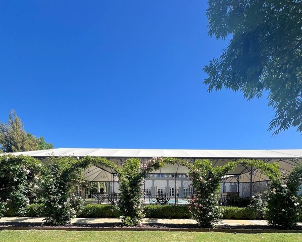 A building with a covered outdoor area, including tables and chairs, under a white canopy.