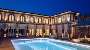 A large pool with a curved edge, surrounded by a courtyard with a building featuring arched windows and columns.