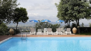 A pool area with lounge chairs and umbrellas, a view of the landscape, and a tiled deck. - Da Angelo (Assisi)