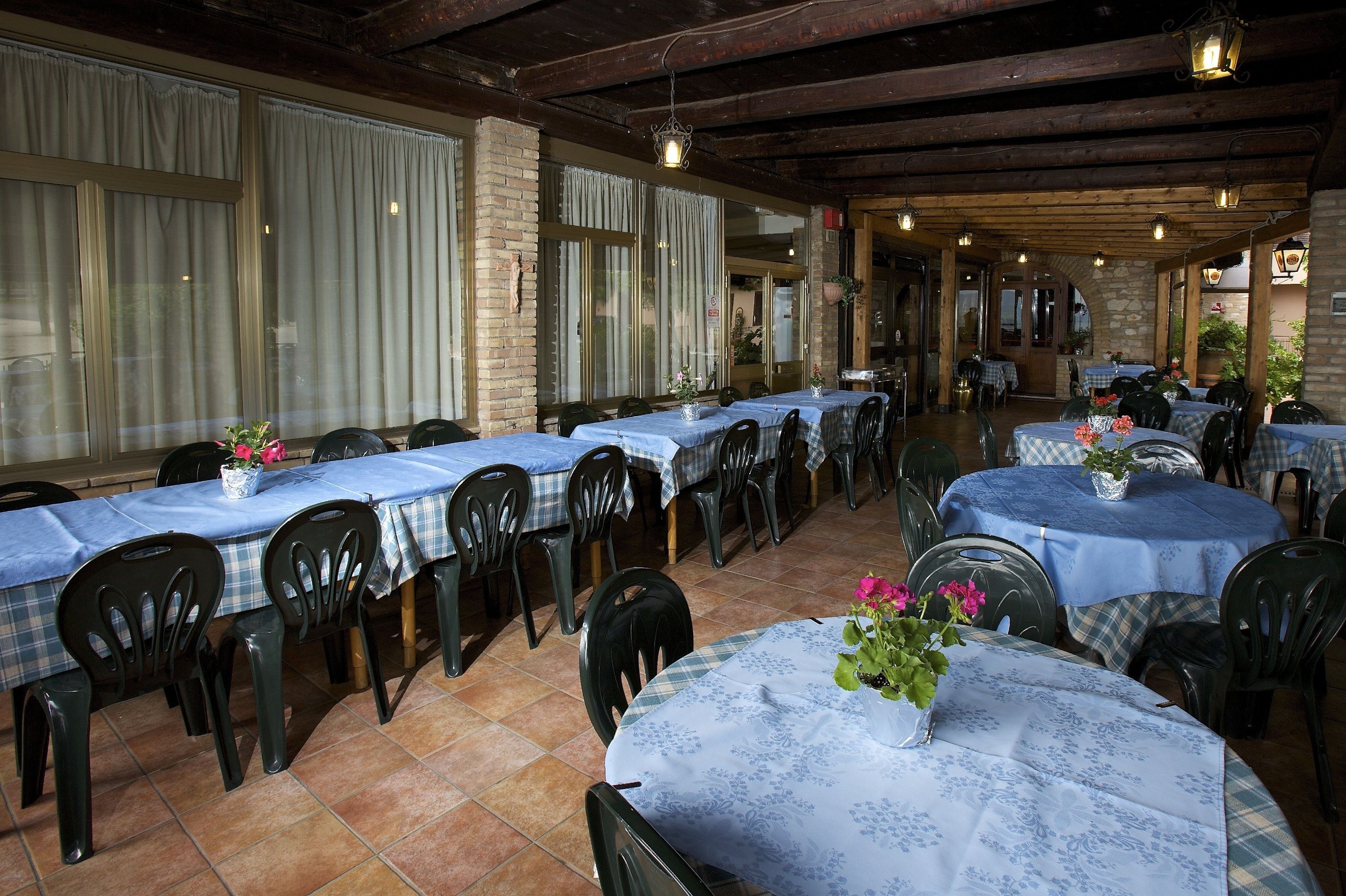 Restaurante com várias mesas cobertas por toalhas azuis, disposto em um espaço interno amplo com vigas de madeira no teto e paredes de tijolo.