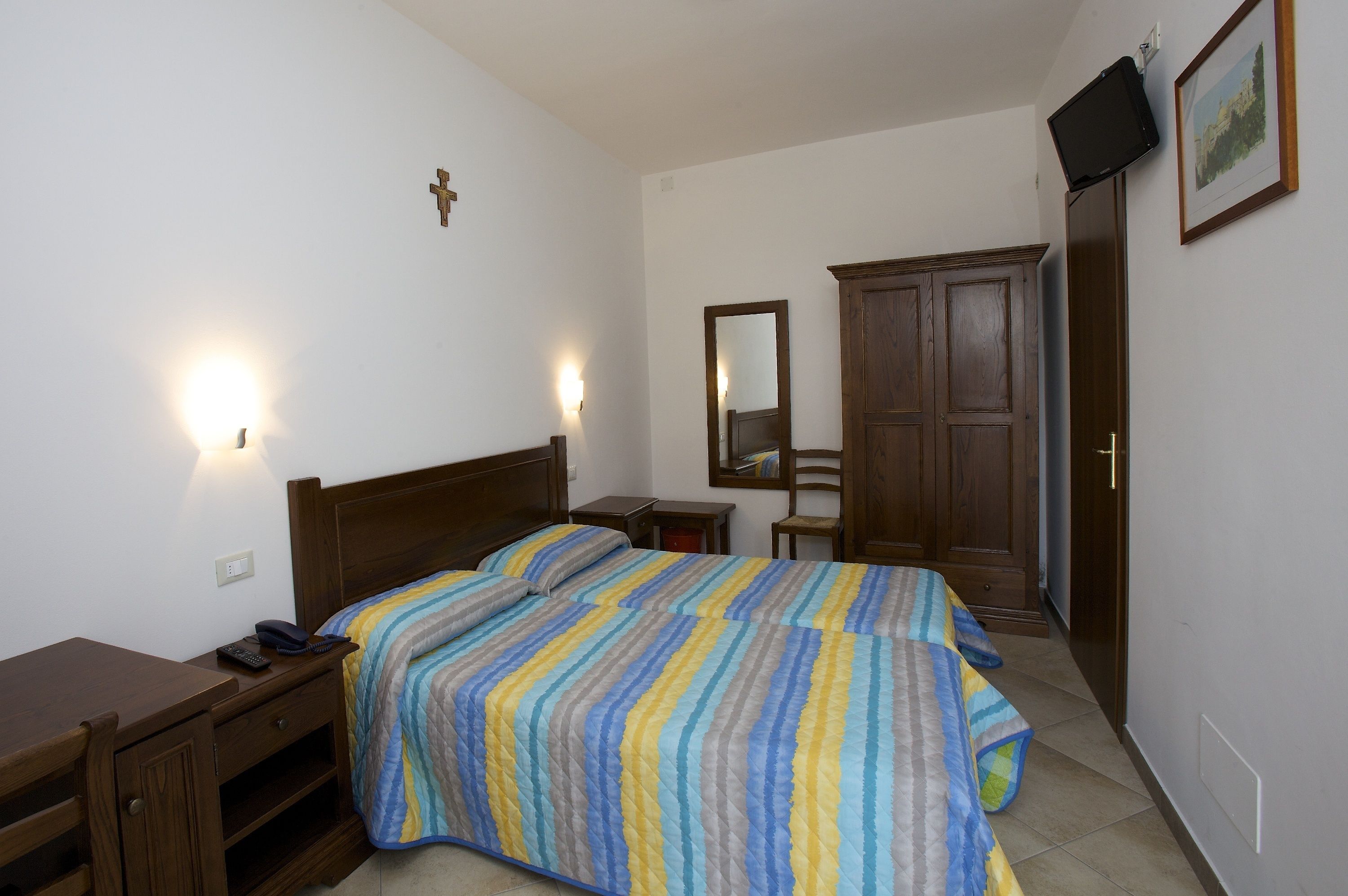 Ein Schlafzimmer mit zwei Betten, einem Holztisch, einem Stuhl, einem Kleiderschrank und einem an der Wand montierten Fernseher.