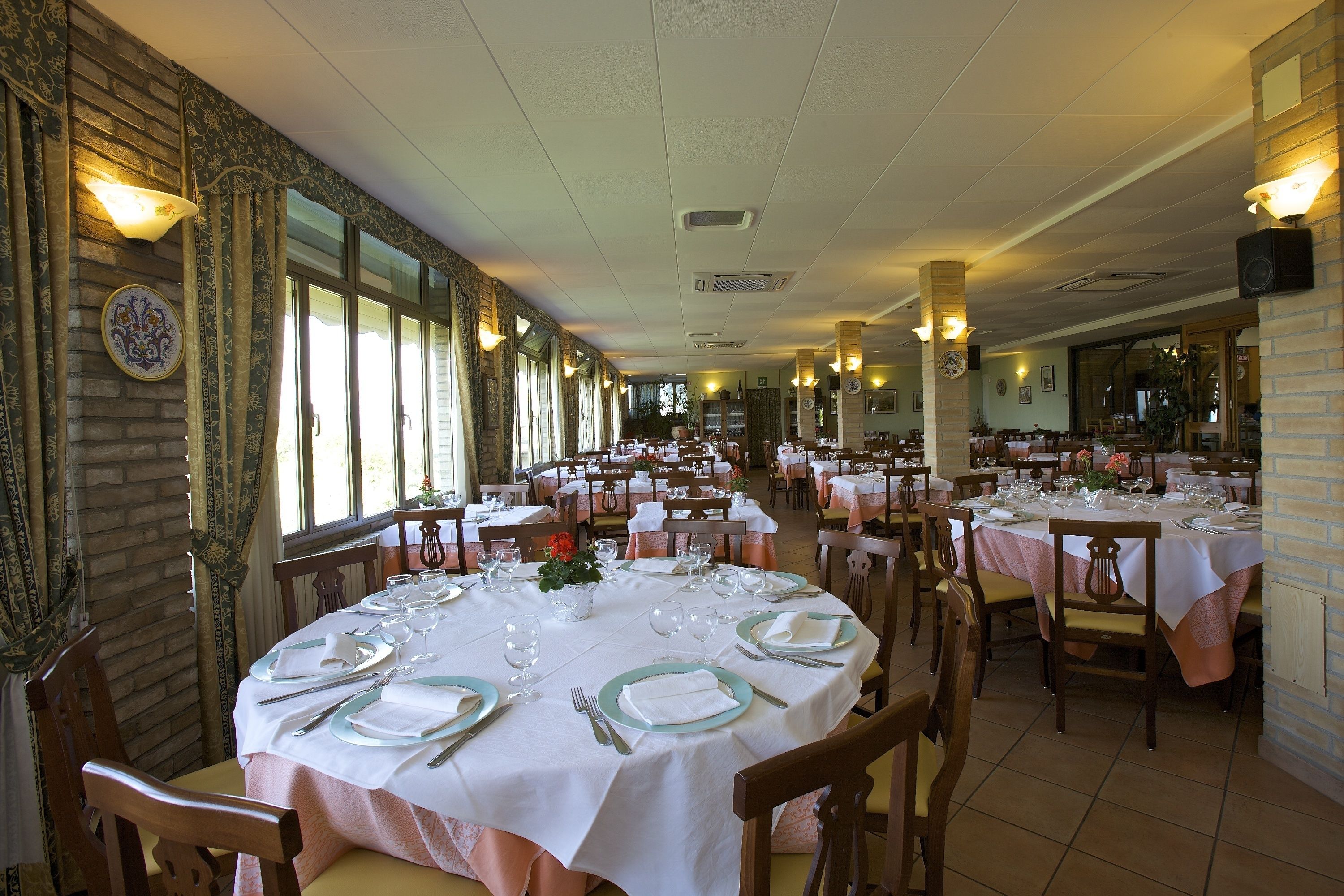 Un restaurant avec des tables rondes dressées pour le repas, agrémentées de nappes blanches et de serviettes vertes.