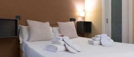 A hotel room with a neatly made bed, pillows, and rolled towels on the bed.