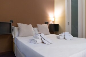 Siisti hotellihuone, jossa sänky on pedattu huolellisesti, tyynyjä on sängyllä ja pyyhkeet on rullattu siististi sängyn päälle.