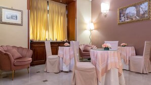 A hotel room with a dining area, a large window with curtains, a wall-mounted lamp, and a framed picture. - Hotel Suite Ares (Naples)