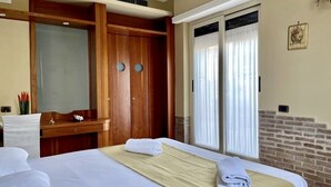 A hotel room with a bed, a wooden wardrobe, a vanity with a mirror, and a window with curtains. - Hotel Suite Ares (Naples)