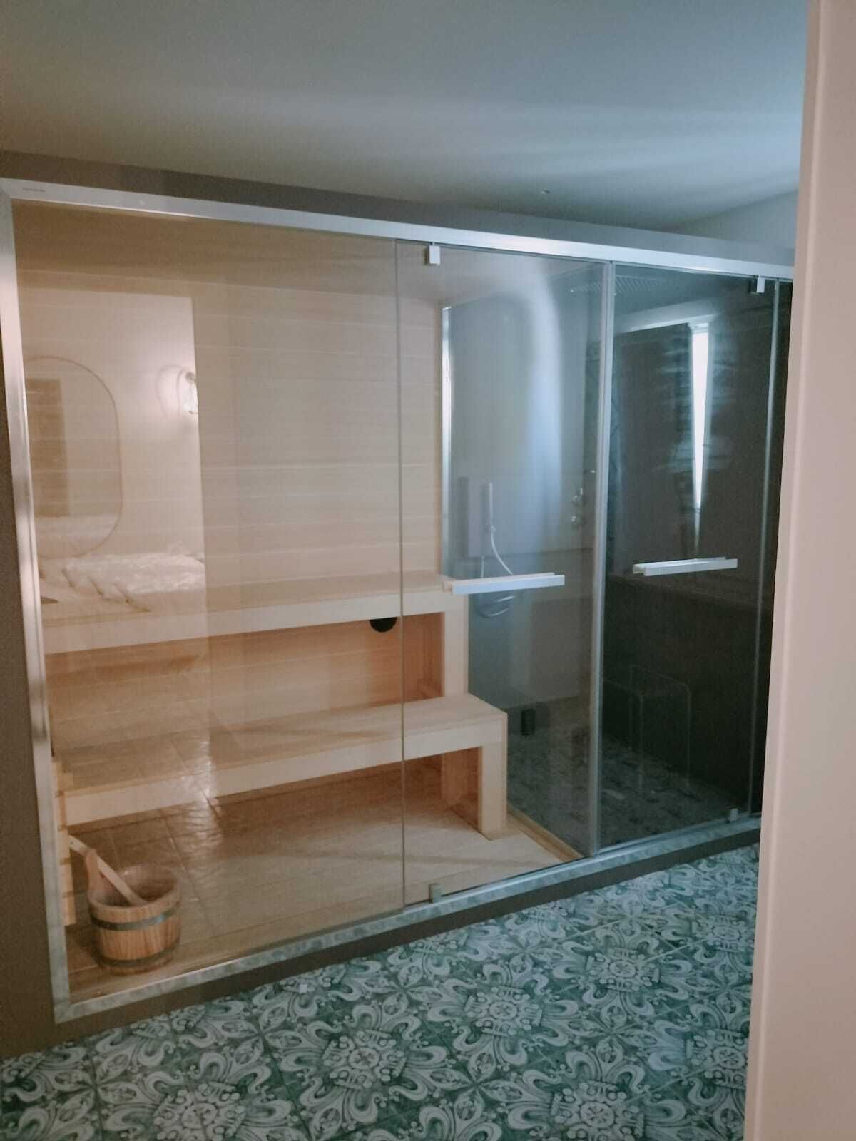 Ein Zimmer mit Duschkabine aus Glas, einer Holzbank und einem gemusterten Boden.