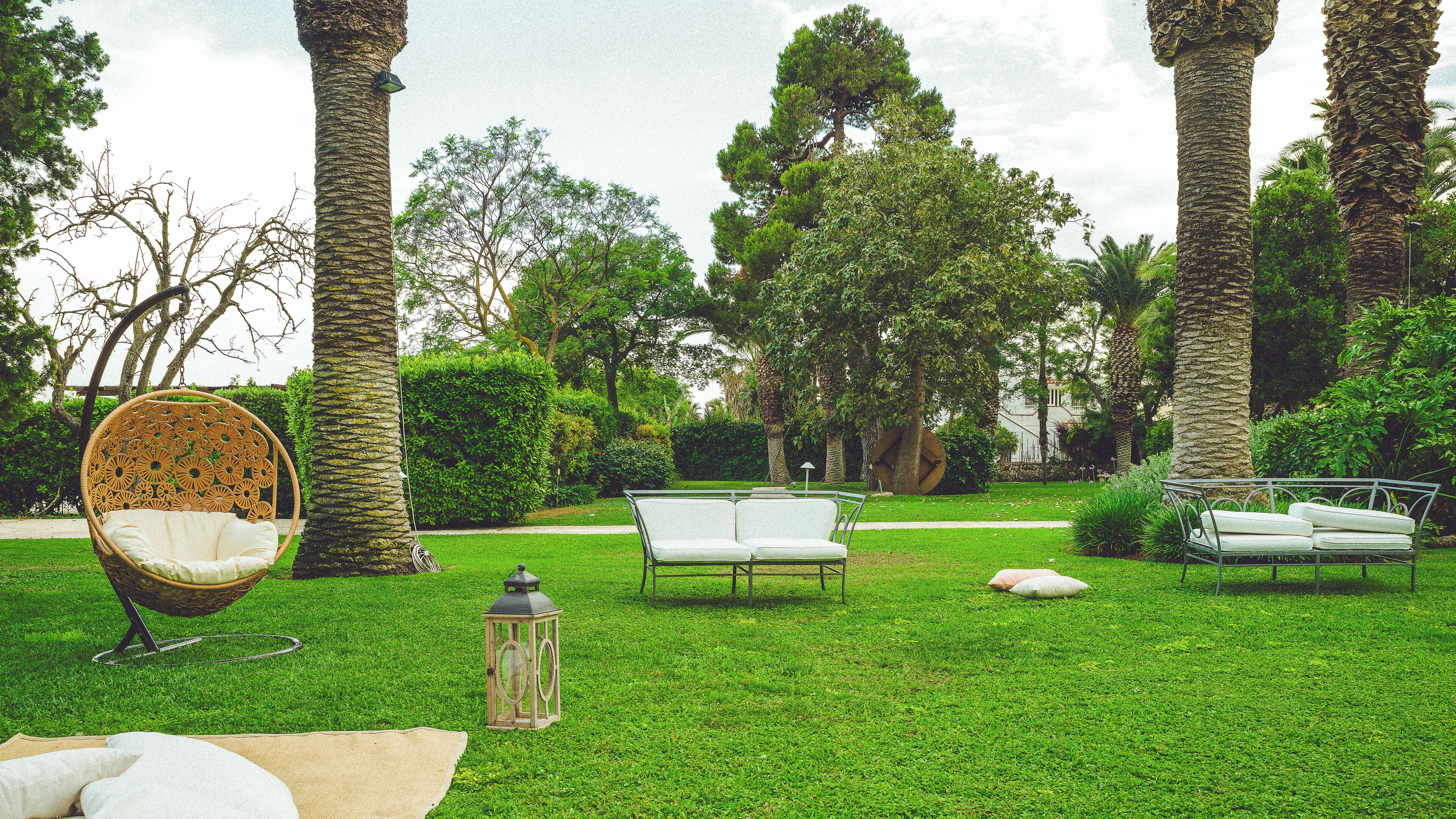 Un jardín con una silla de mimbre, un banco de metal y un farol.