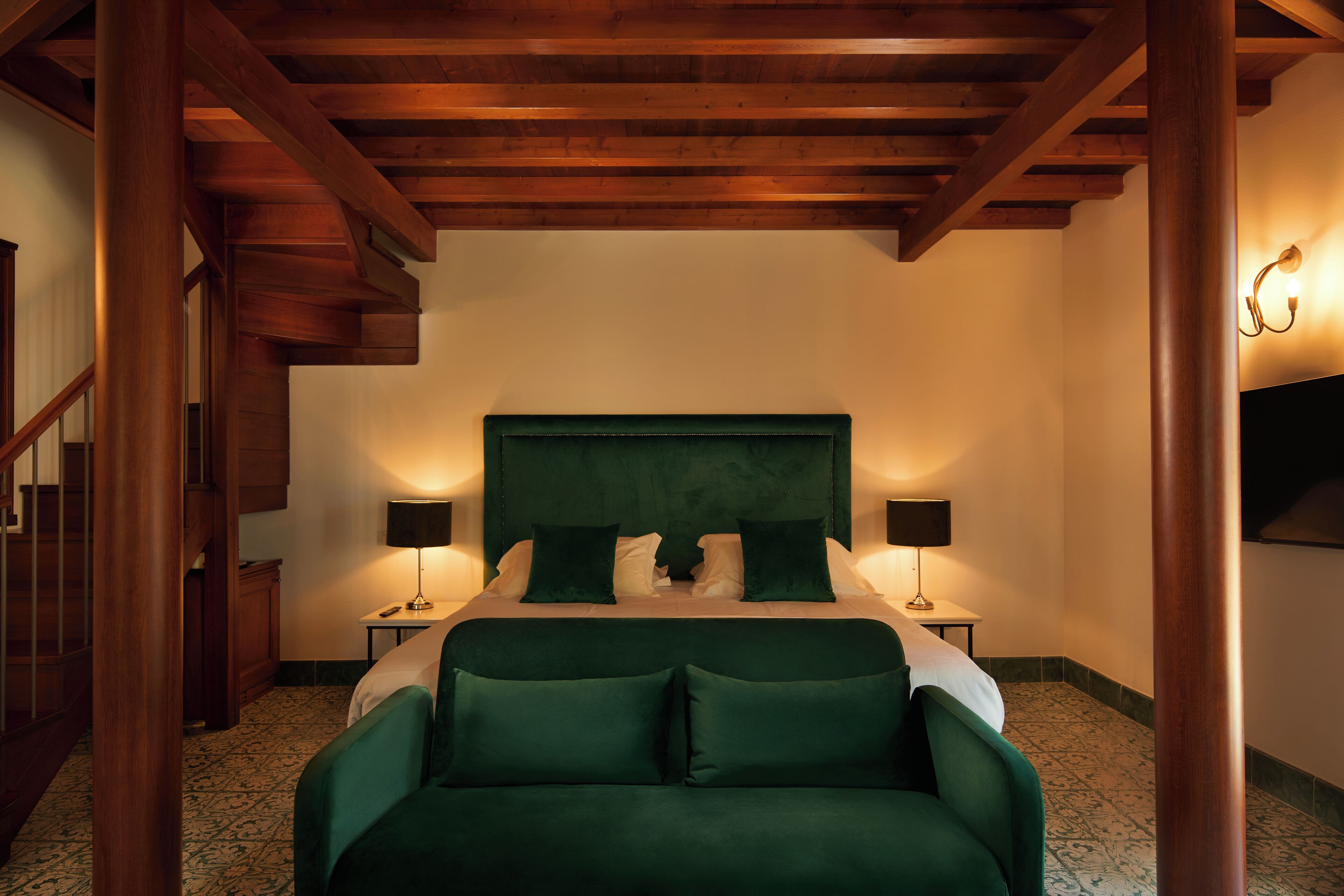 A bedroom with a large bed, two bedside tables, a headboard, and a staircase in the background.